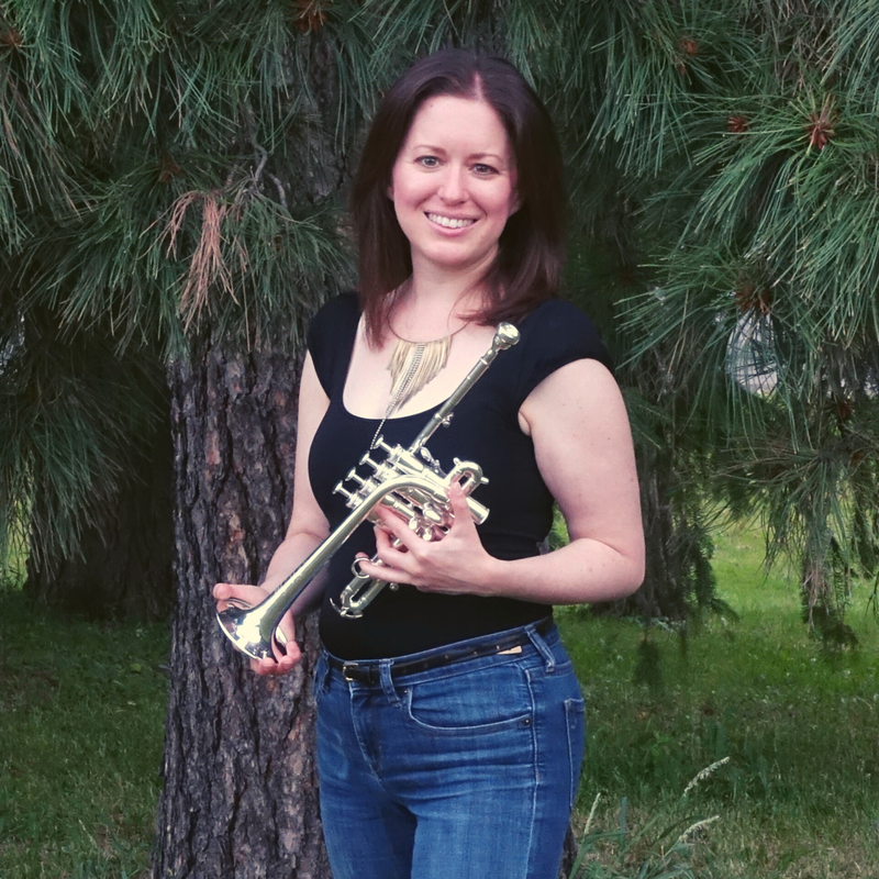 Woman holding a trumpet in front of a pine tree.